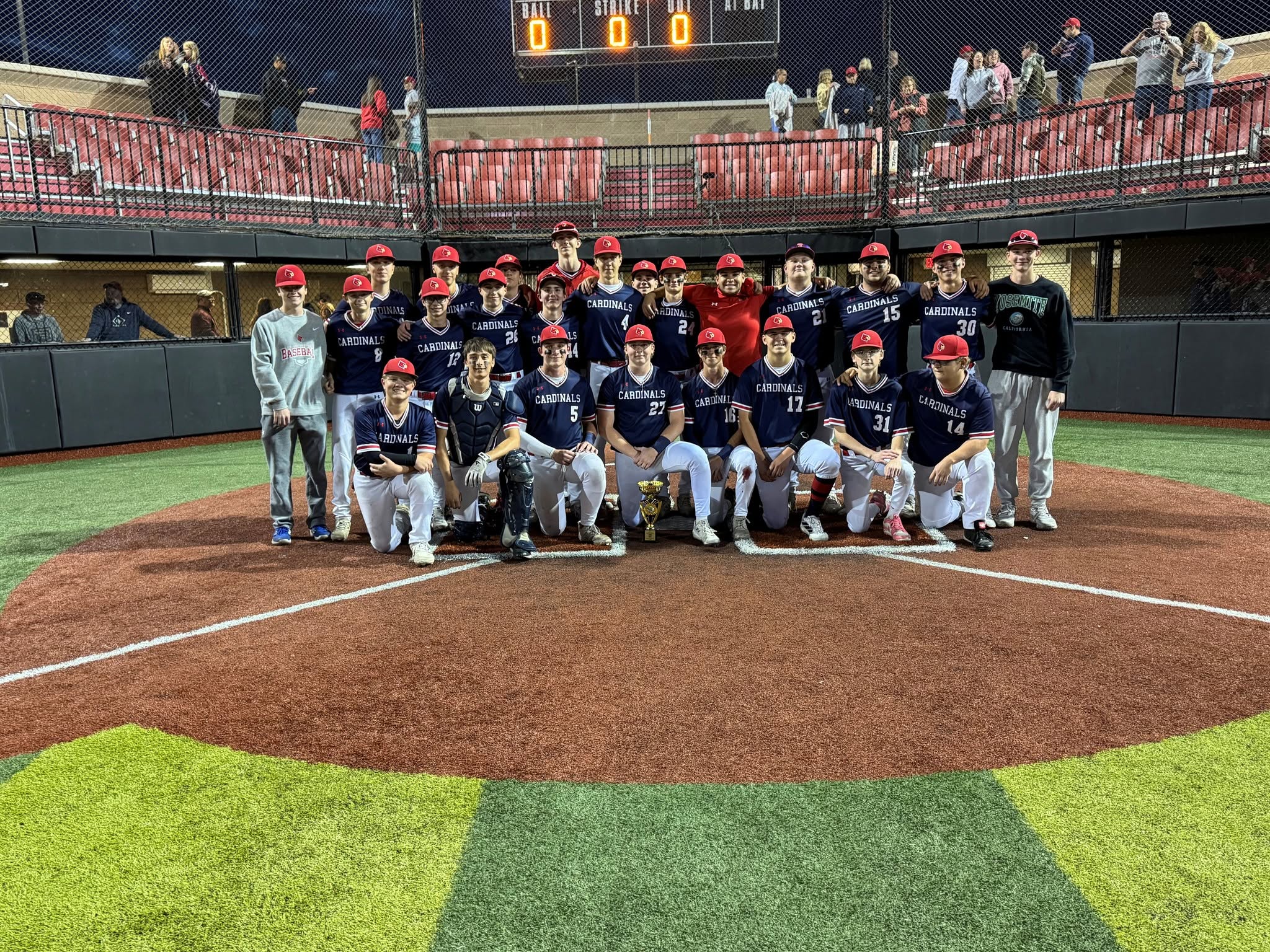 Cardinals baseball players posing with a trophy on a baseball field.